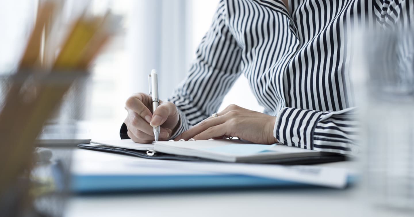 A close-up of a woman's hands writing in a planner.