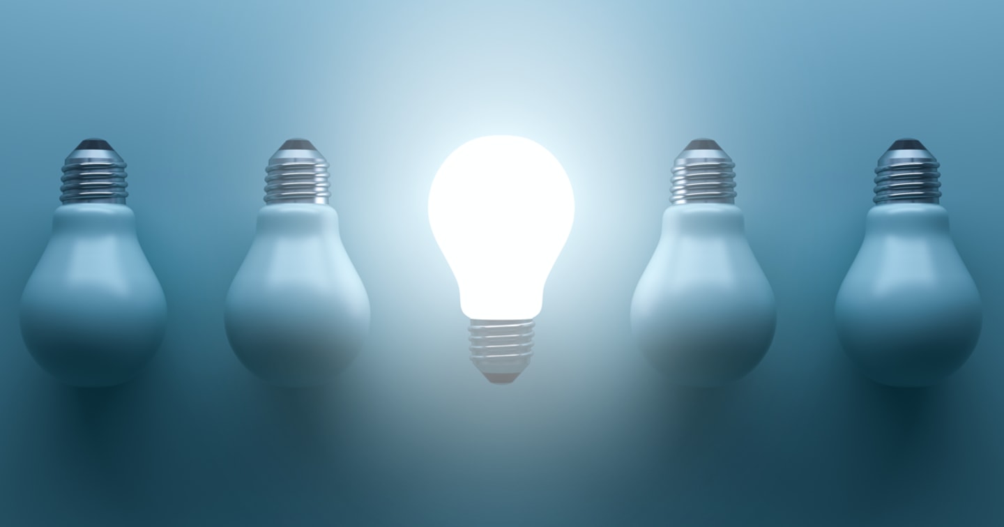 A group of lightbulbs all pointed down and unlit except for the one in the center that is upwards and lit.