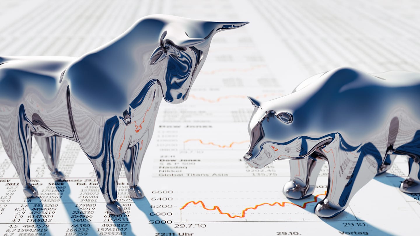 Metallic bull and bear figurines standing on stock market charts.
