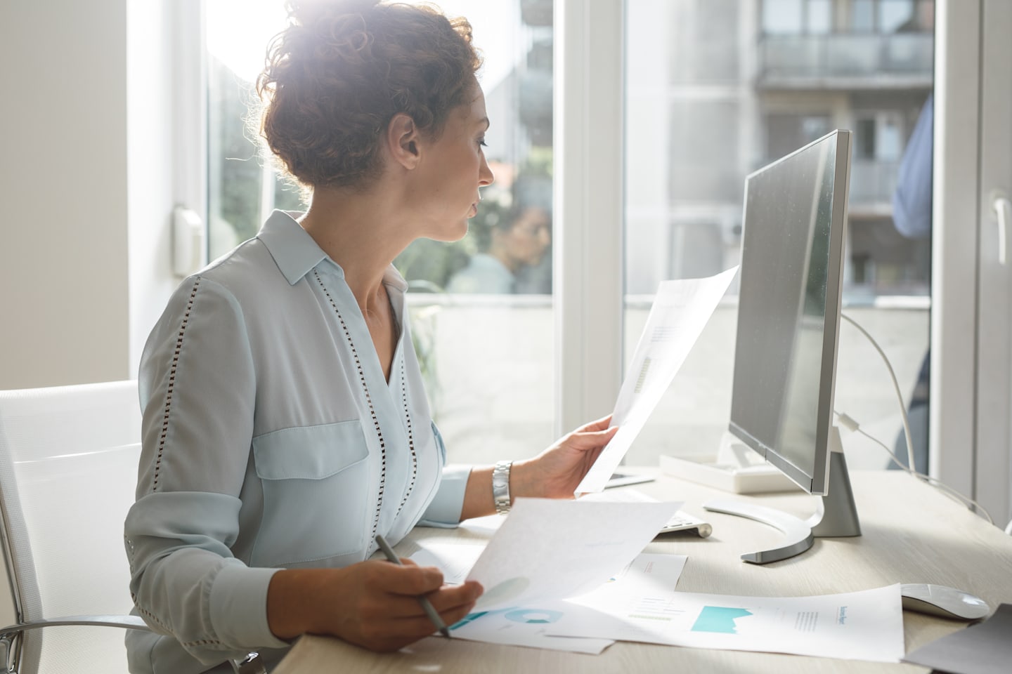 Woman looking over paperwork by a computer.