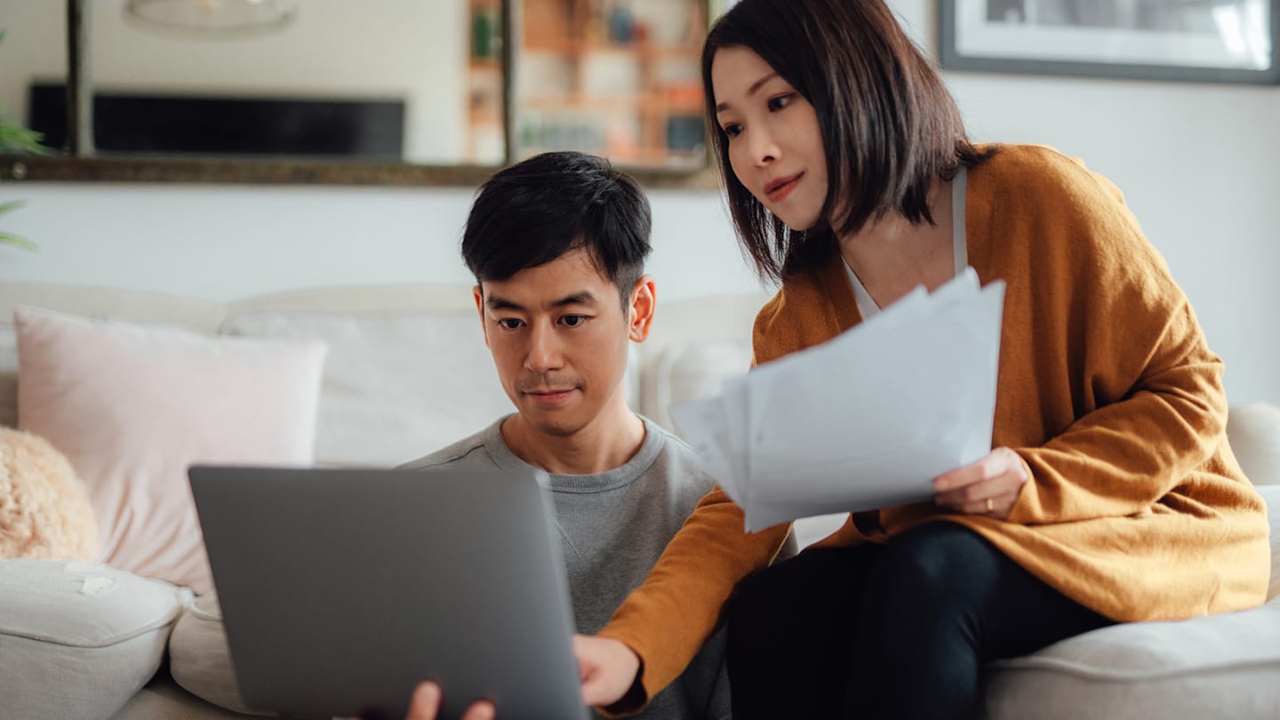 Couple in living room with laptop and paperwork.