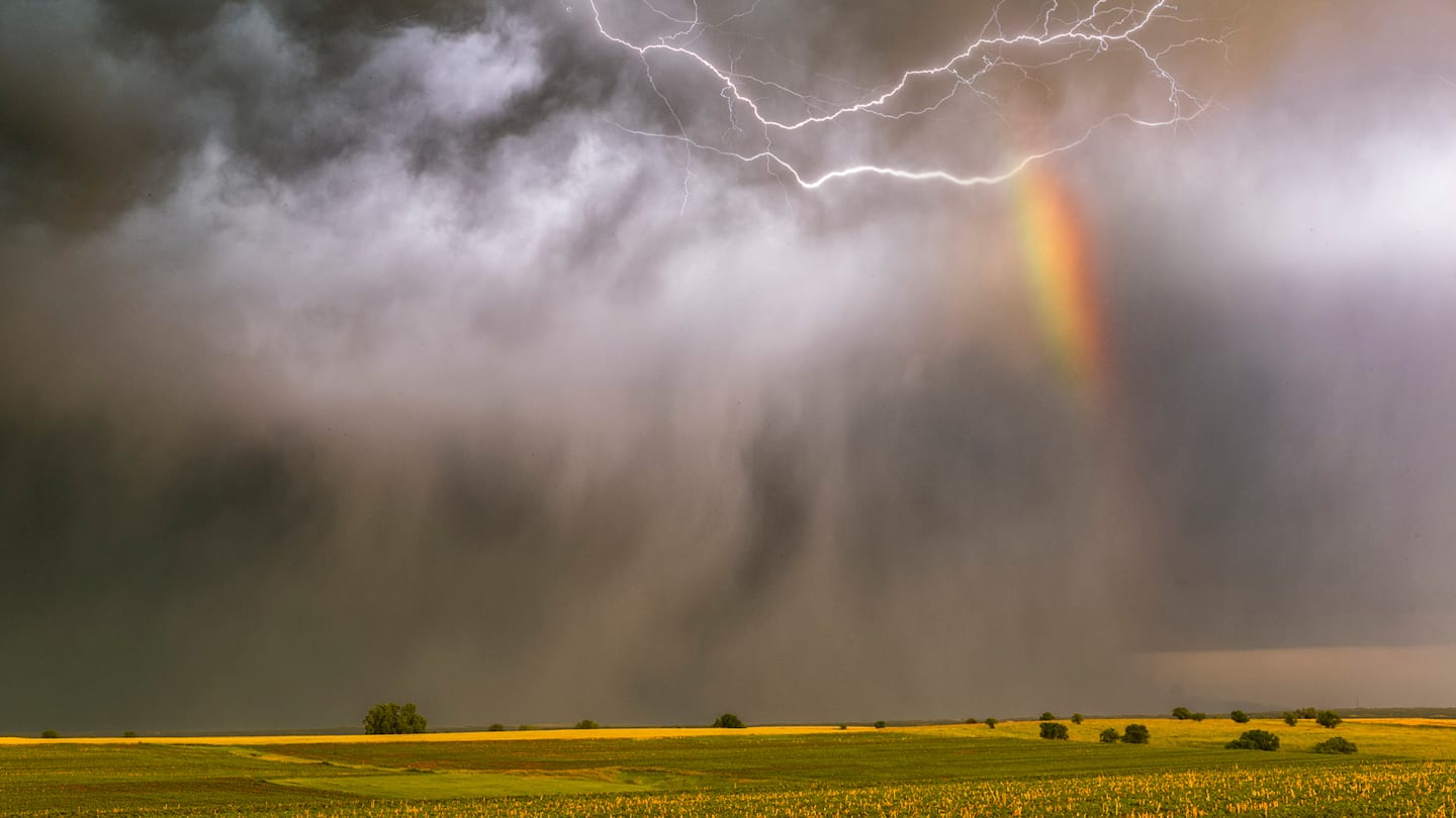 Rainbow breaking through storm clouds over open land.