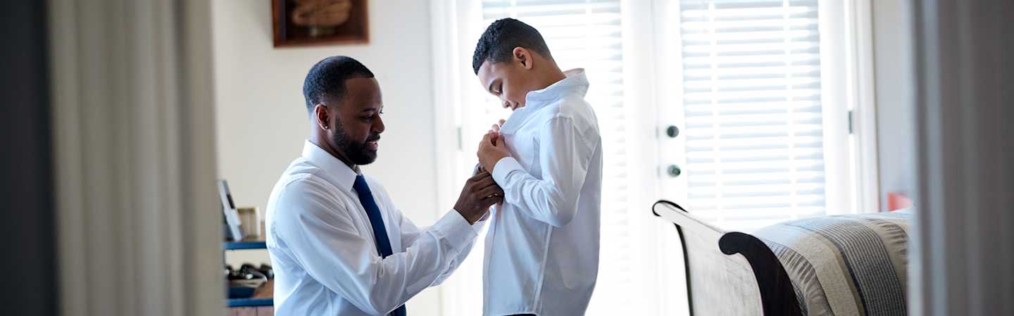 Father helping son fix shirt.