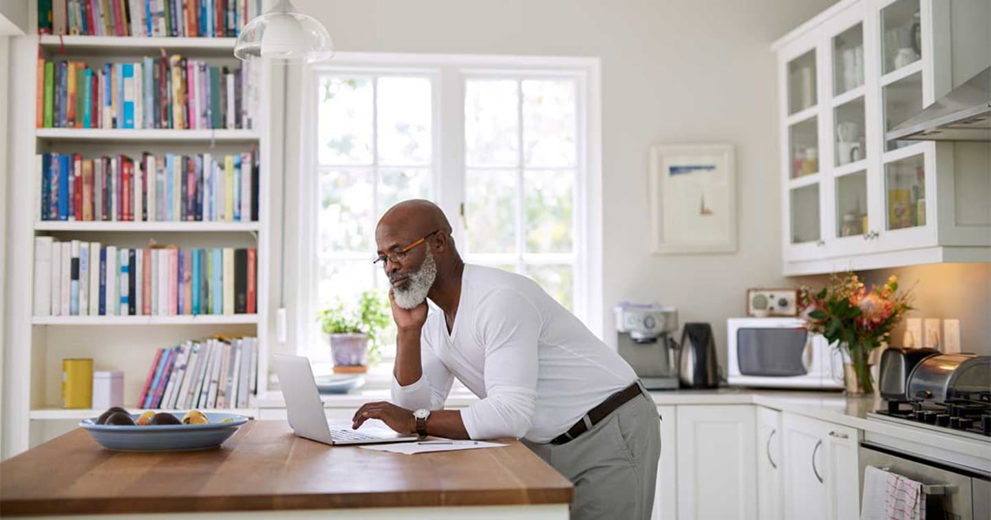 A man leaning over his kitchen island looking at his laptop.
