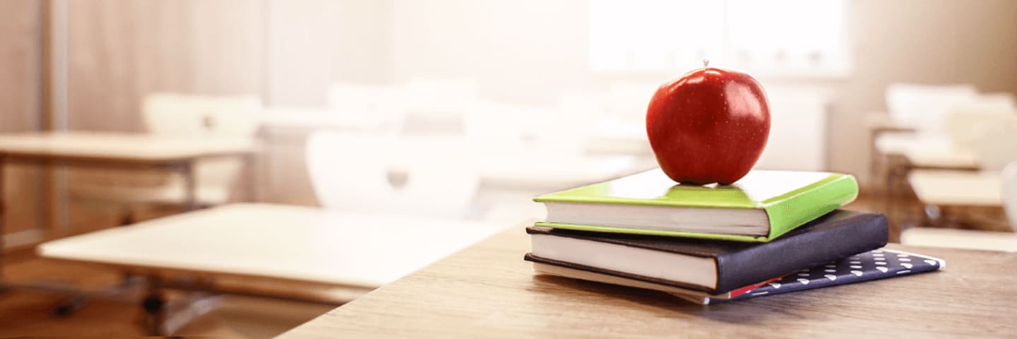 An apple sitting on top of two textbooks in a classroom.