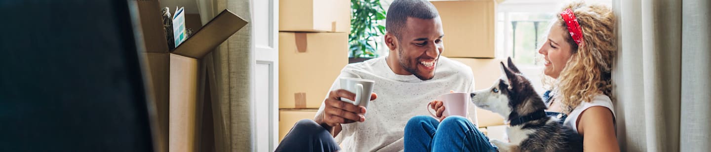 A young couple having coffee on their porch with moving boxes behind them.