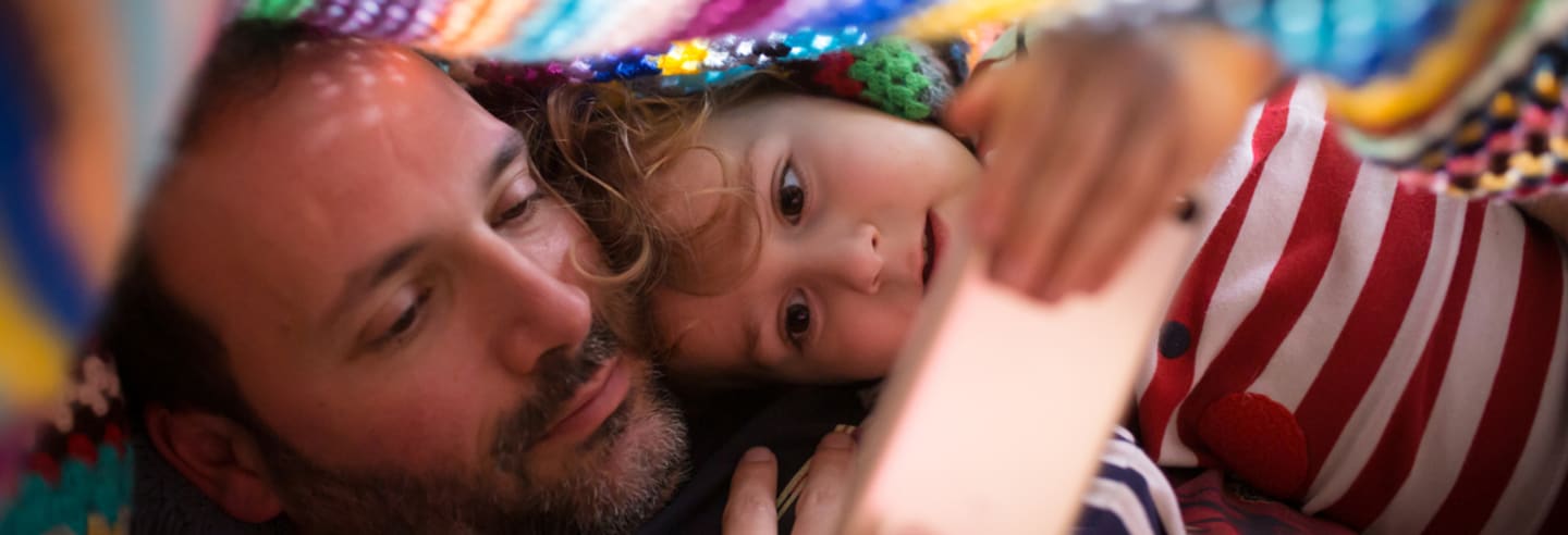 A father and his daughter snuggled together looking at an electronic device.