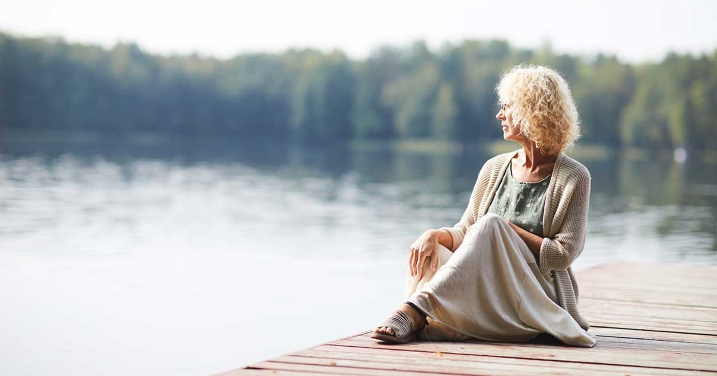An older women sitting a wood dock looking out over a body of water.