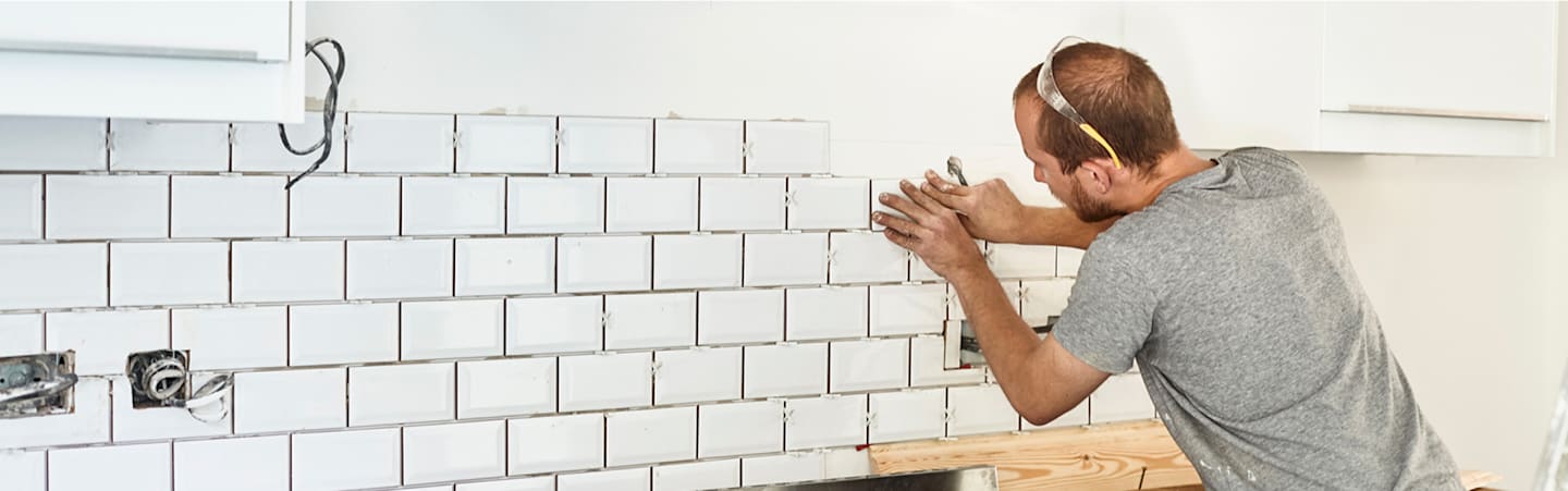 Man installing tile in kitchen.