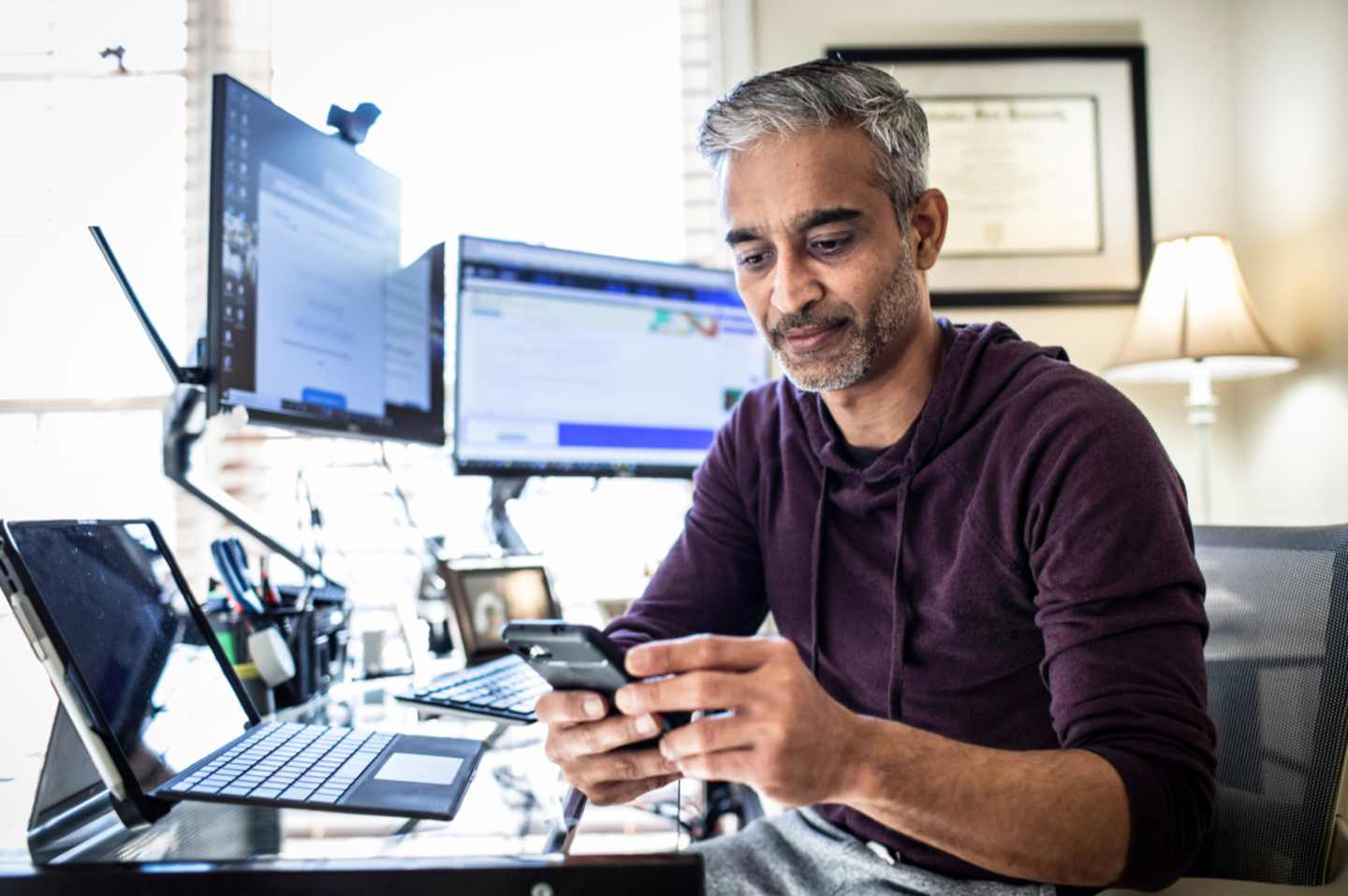 Man at computer desk set up looking at phone.