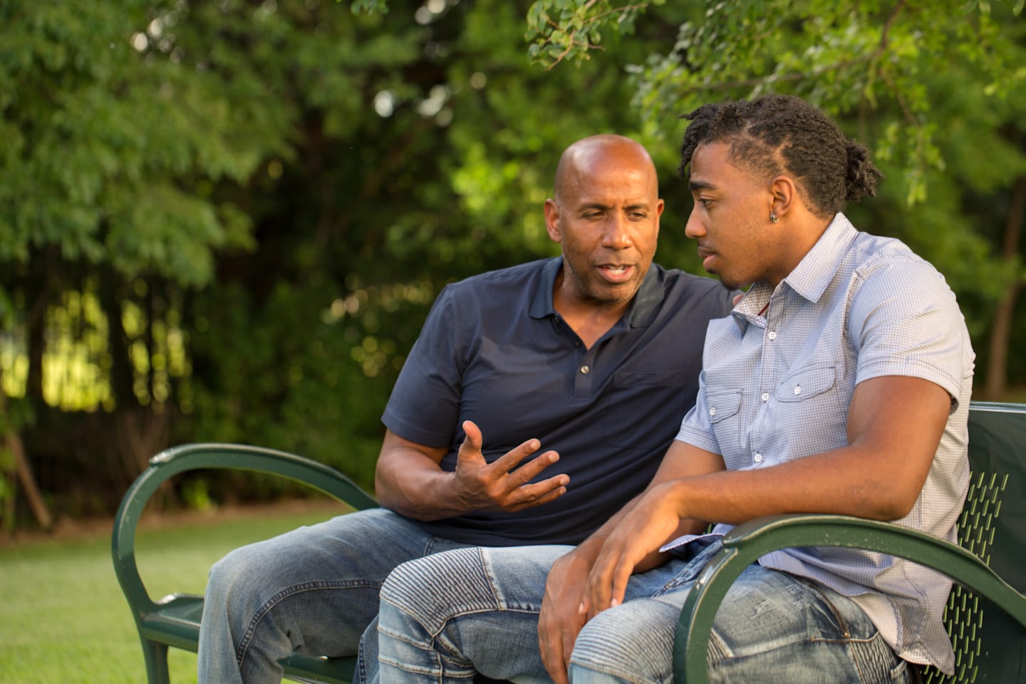 Father speaking with son on park bench. 
