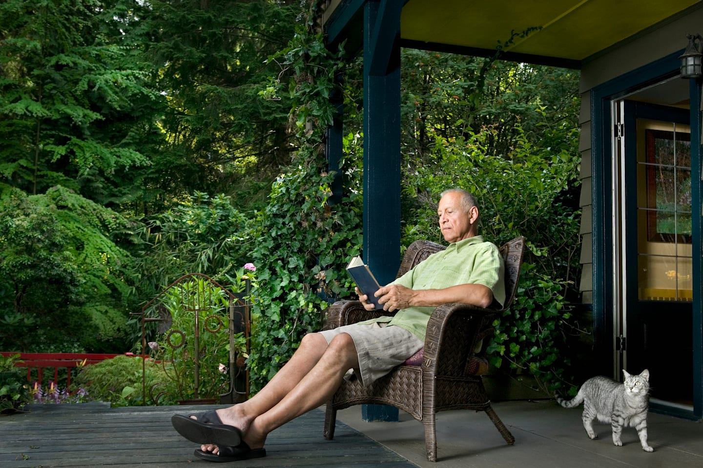 Older man sitting on front porch of house in summer time. 