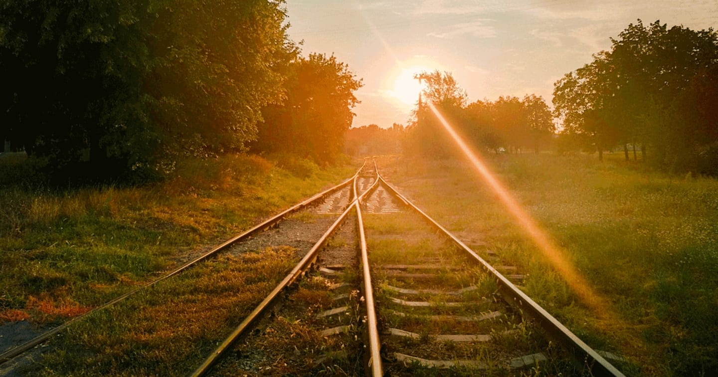 The sun rising over railroad tracks in the country.