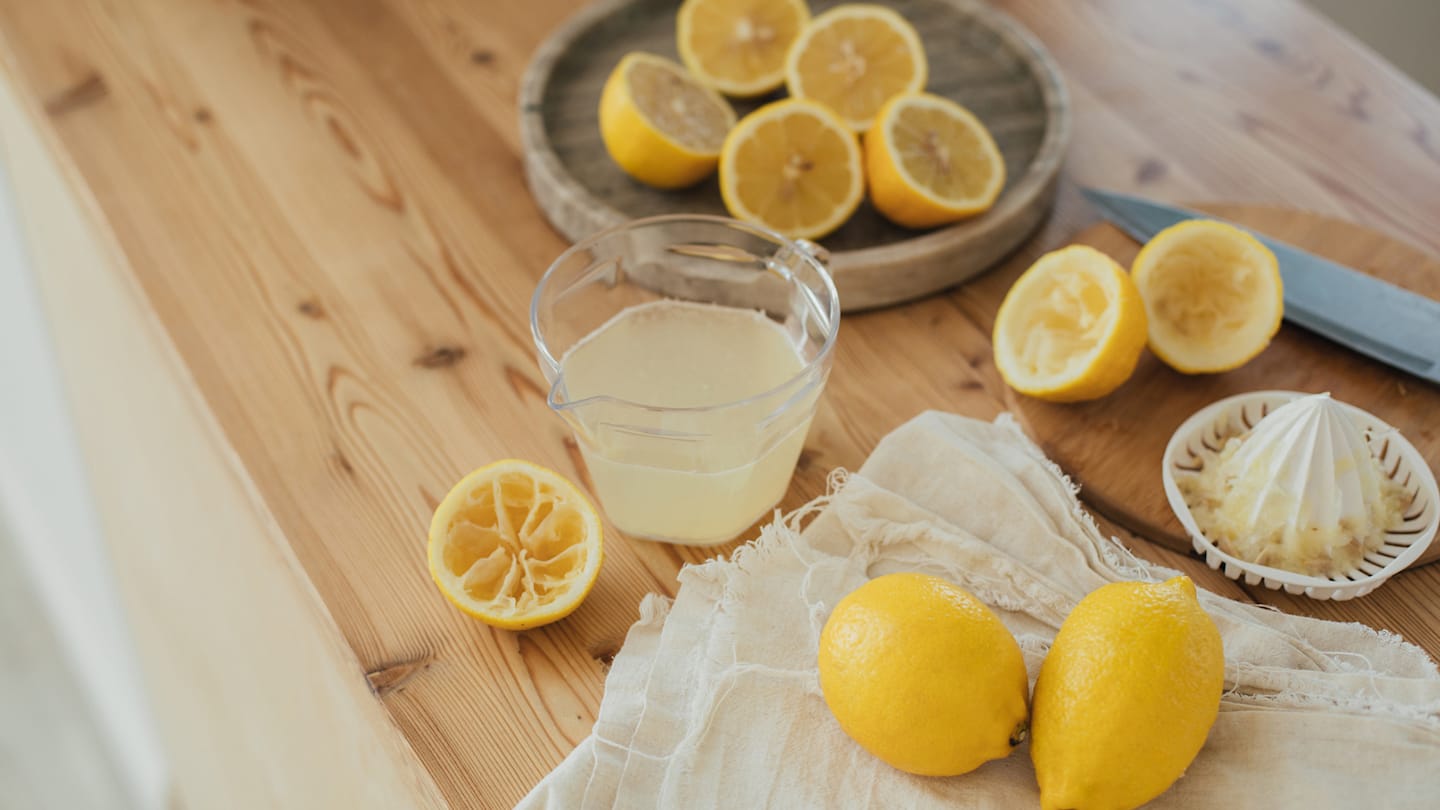 Glass of lemonade on kitchen table with several squeezed lemons.