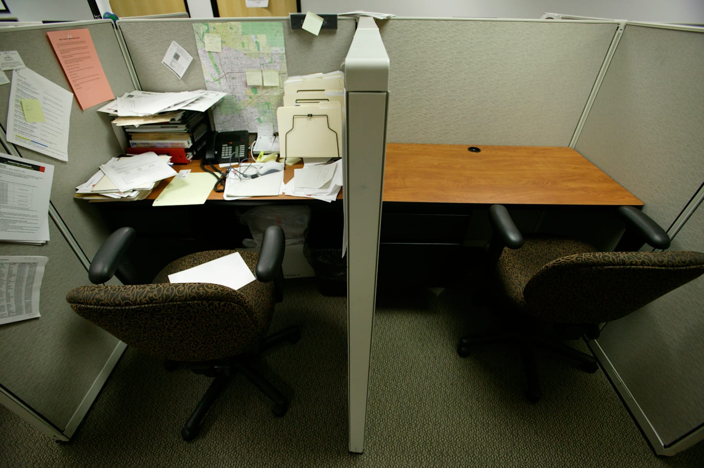 Cluttered desk next to an empty desk in office setting.