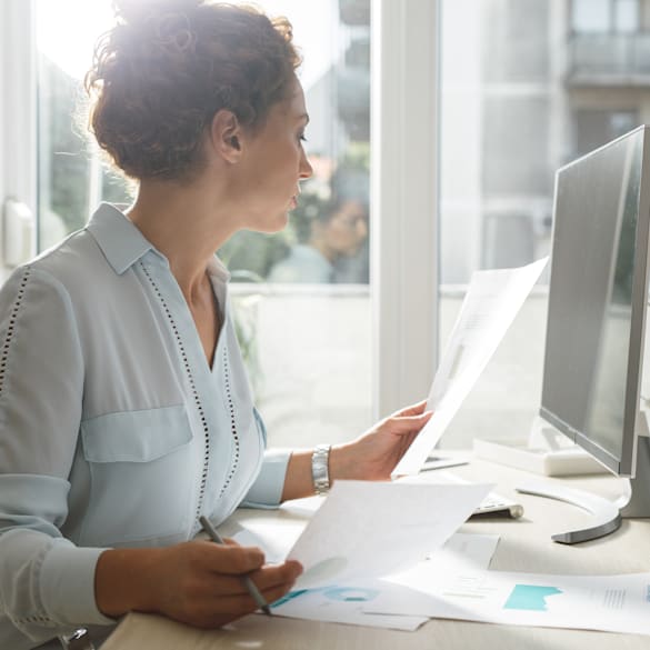 Woman looking over paperwork by a computer.