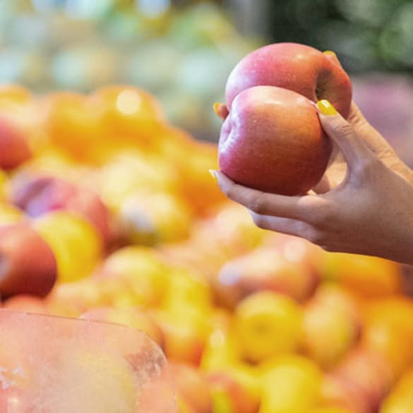 A woman choosing between two apples in the supermarket.