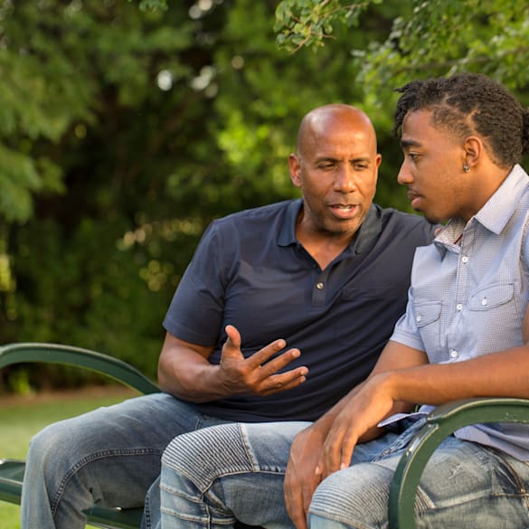 Father speaking with son on park bench.