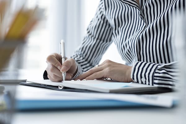 Person writing in a notebook with a pen