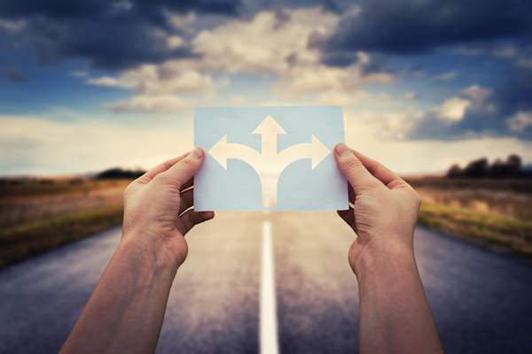 Hands holding multi-direction arrows on an open expanse of road.