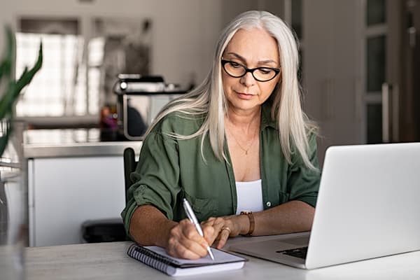 Woman taking notes on paper next to laptop.