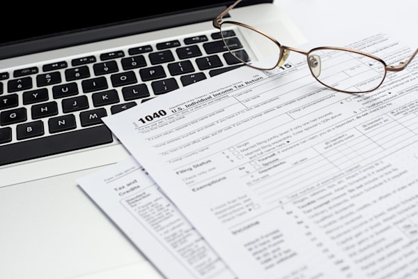 An IRS 1040 form by a computer. A pair of glasses rest on top of the form.