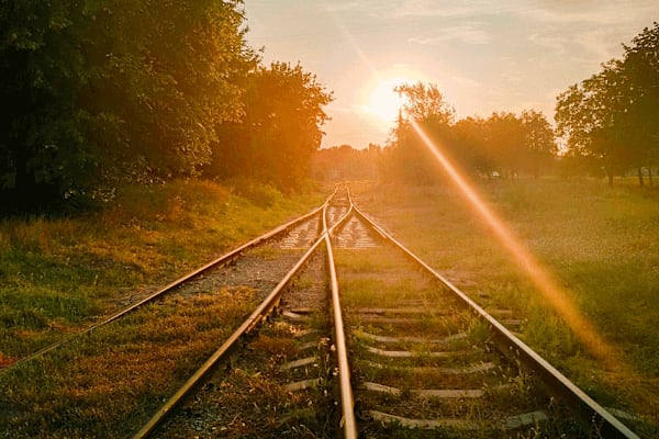 Image of a sunrise glowing over to railroad tracks that converge in the distance.